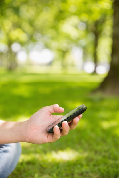 Frau, die einen Text auf Smartphone im Park sendet