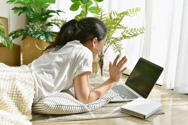 Frau, die einen Videoanruf macht, der auf einem Laptop-Computer chattet Asiatisches Mädchen lächelt und winkt zu Hause mit grünen Naturbaumpflanzen Künstliche Zimmerpflanze für Zuhause und Wohnzimmer