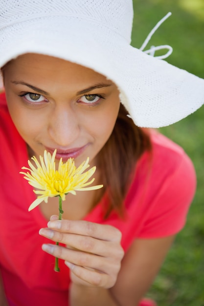Frau, die einen weißen Hut beim Riechen einer Blume beim aufwärts schauen trägt