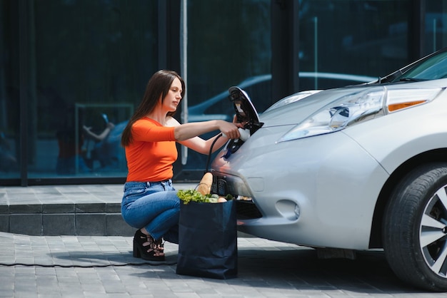 Frau, die Elektroauto an der elektrischen Tankstelle auflädt