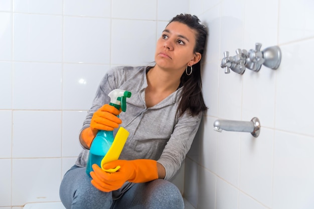 Frau, die es satt hat, das Badezimmer zu reinigen, sitzt frustriert in der Badewanne mit Reinigungsmitteln