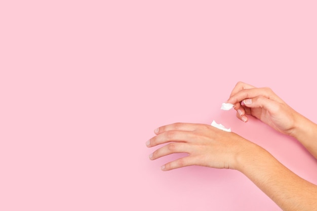 Frau, die Feuchtigkeitscreme Hände Creme auf einen rosa Hintergrund mit Kopienraum setzt