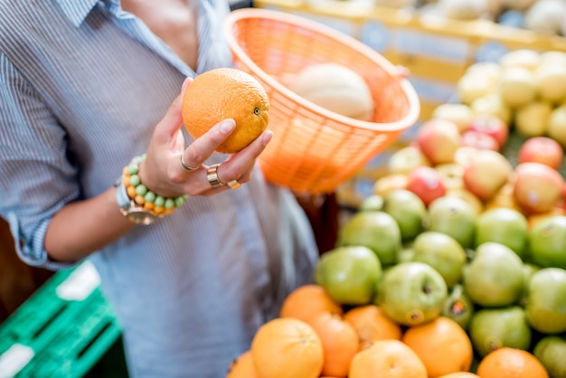 Frau, die frische Orangen mit Korb auf dem Lebensmittelmarkt mit Obst und Gemüse wählt