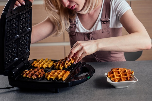 Frau, die frische Waffeln aus dem Waffeleisen in der Küche belgische Waffeln nimmt?