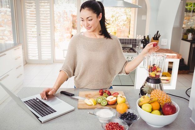 Frau, die Fruchtsaft beim Arbeiten an Laptop zubereitet