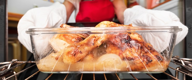 Frau, die gebratenes Huhn vom Ofen nimmt. Im Ofen kochen.