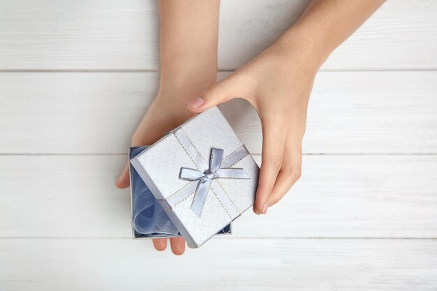 Frau, die Geschenkbox auf hölzernem Hintergrund öffnet