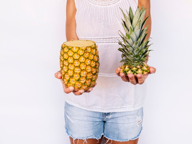 Frau, die geschnittene Ananas gegen weiße Wand hält