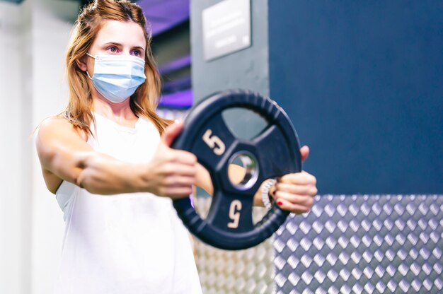 Frau, die Gewichte im Fitnessstudio mit einer Maske hebt