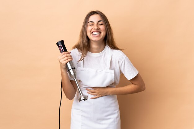 Frau, die Handmixer über isolierte Wand viel lächelnd verwendet