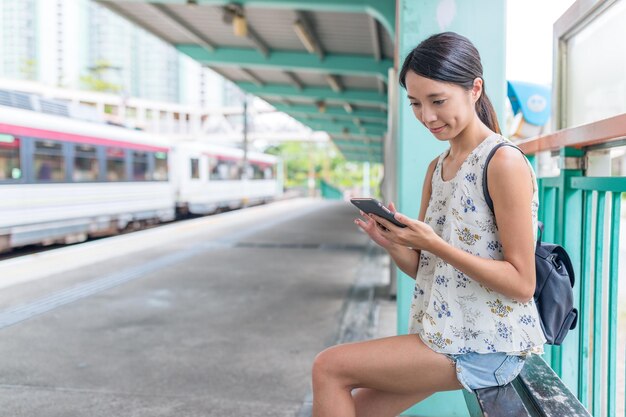 Frau, die Handy benutzt und in der Trsin-Station wartet