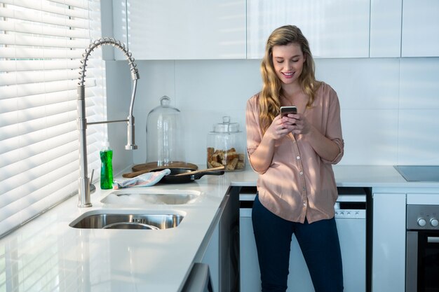 Frau, die Handy in der Küche benutzt