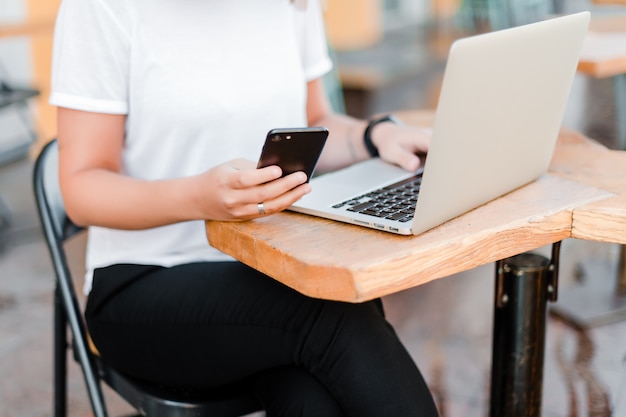 Frau, die Handy und Laptop im Café verwendet