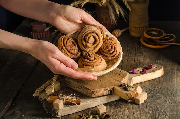 Frau, die hausgemachte Zimtbrötchen in einer Weidenplatte gegen einen dunklen Hintergrund, dunkles Artlebensmittelfoto dient