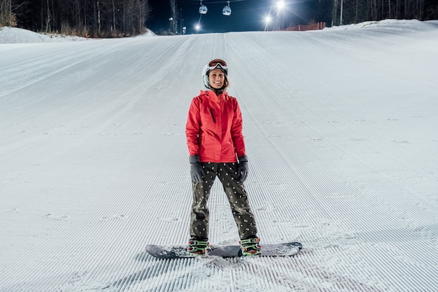Frau, die helm mit snowboard auf der skipiste trägt. abendreiten