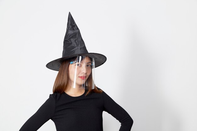 Frau, die Hexenkostüm und Maskengesichtsschild für Halloween trägt