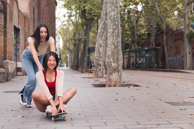 Frau, die ihre Freundin auf einem Skateboard sitzend schiebt