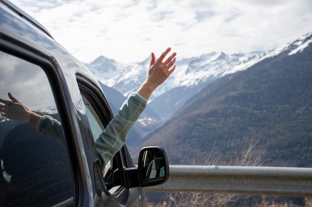 Frau, die ihre Hand aus dem Fenster ihres Lieferwagens streckt und den Blick auf die schneebedeckten Berge genießt
