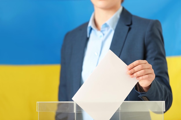 Frau, die ihre Stimme in die Wahlurne gegen die ukrainische Flagge legt, Nahaufnahme Platz für Text