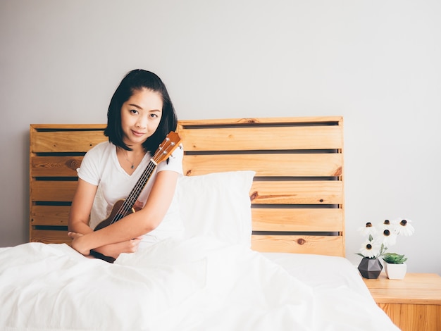 Frau, die ihre Ukulele in ihrem gemütlichen Schlafzimmer hält.