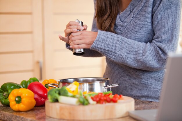 Frau, die ihrem Gemüseeintopf Pfeffer hinzufügt