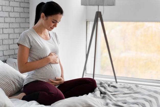 Frau, die ihren Bauch beim Sitzen im Bett hält