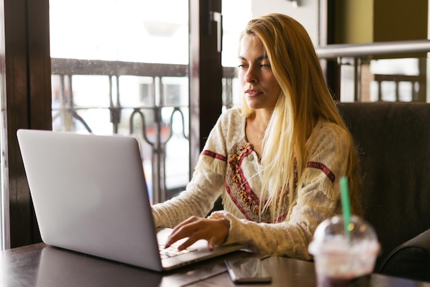 Foto frau, die ihren computer drinnen benutzt, während sie etwas trinkt.