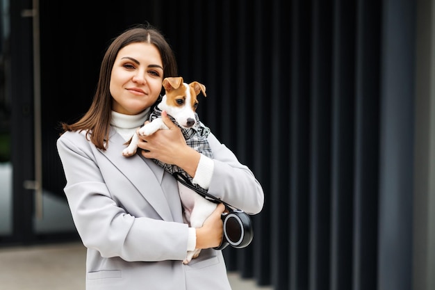 Frau, die ihren flauschig ausgebildeten reinrassigen Jack Russell Terrier-Hund umarmt, der im Anzug für Hunde im Freien gekleidet ist