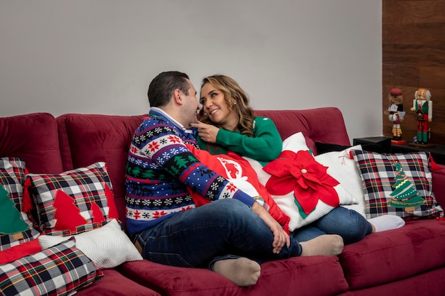 Frau, die ihren glücklichen Ehemann in einer Weihnachtsnacht ansieht, die mit Weihnachten im Sessel sitzt