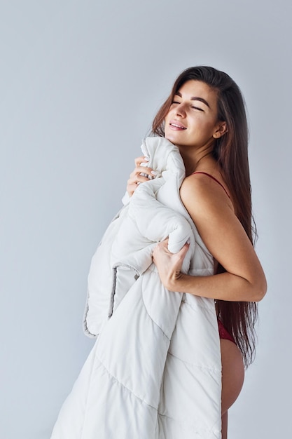 Frau, die ihren Körper mit einem Handtuch im Studio vor weißem Hintergrund bedeckt.