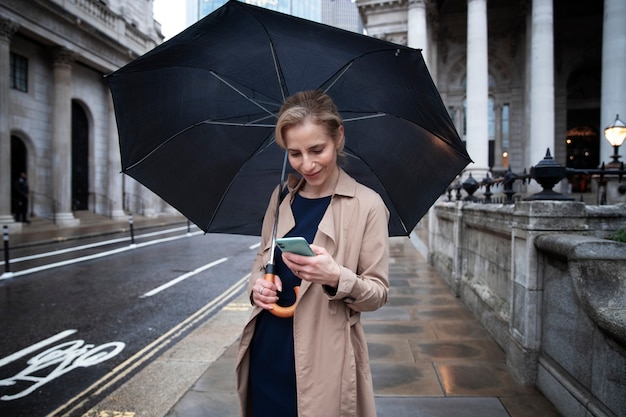 Frau, die ihren Regenschirm hält und jemanden anruft, während sie draußen ist, wenn es regnet