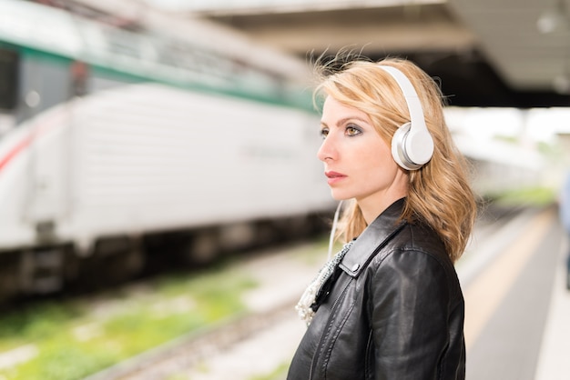 Frau, die ihren Zug während hörende Musik wartet