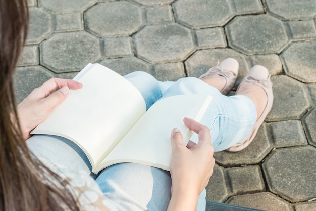 Frau, die im allgemeinen Park für das Lesen eines Buches sitzt