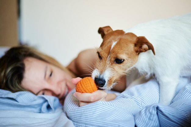 Frau, die im Bett liegt und mit ihrem Hund spielt, entspannt sich am Wochenende am Morgen