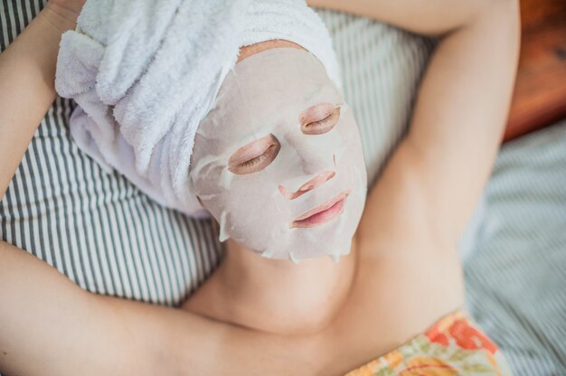 Frau, die im Bett mit einer Gesichtsmaske entspannt