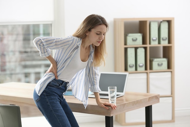 Frau, die im Büro unter Rückenschmerzen leidet Symptom einer schlechten Körperhaltung