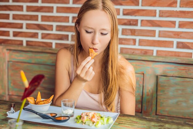 Frau, die im Café isst. Lebensstil. Das Gericht besteht aus Salat, Samosa und verschiedenen Saucen.