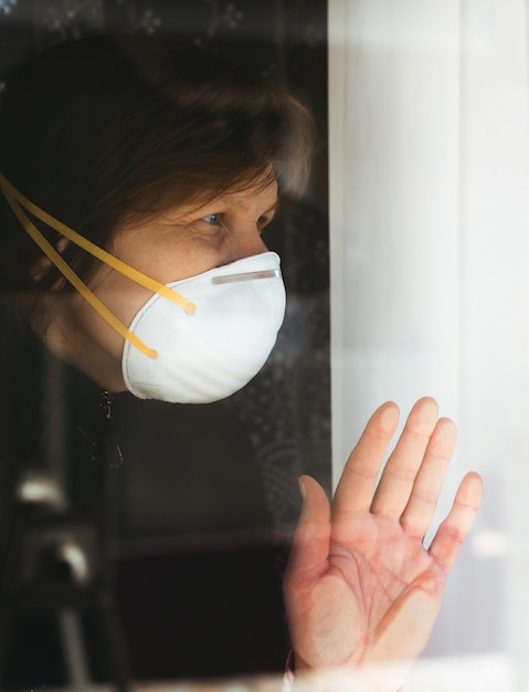 Frau, die im Fenster mit Maske auf Gesicht sitzt