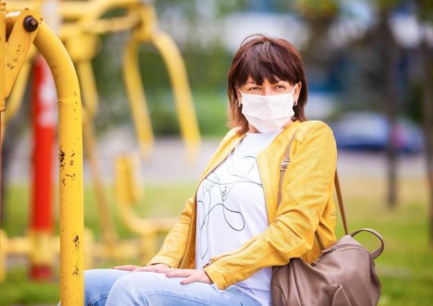 Frau, die im Frühlingspark trägt, der die schützende weiße medizinische Maske trägt