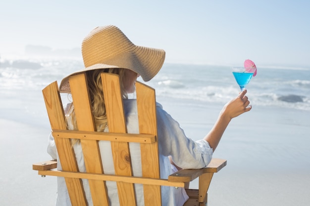 Frau, die im Klappstuhl durch das Meer hält Cocktail sich entspannt