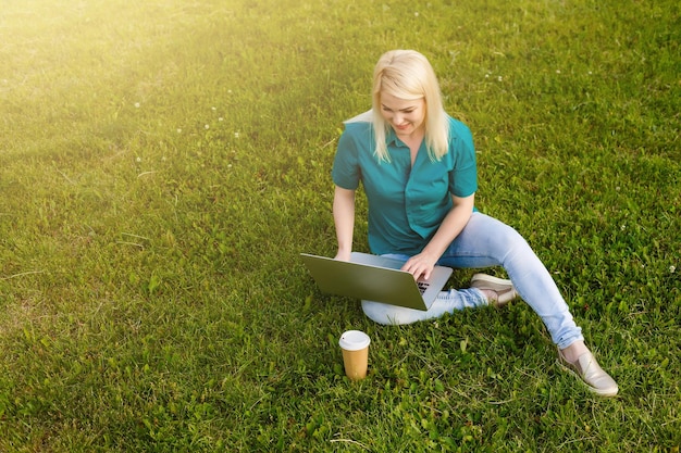 Frau, die im Sommer einen Job mit einem Laptop in einem städtischen Park sucht