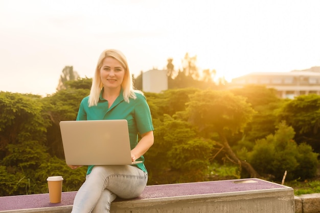 Frau, die im Sommer einen Job mit einem Laptop in einem städtischen Park sucht