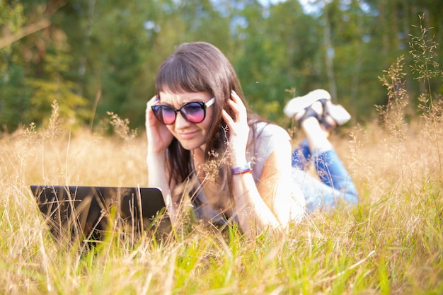 Frau, die im Sommer mit einem Laptop mitten auf einem Feld arbeitet