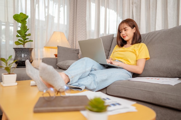 Frau, die im Urlaub auf einem Sofa sitzt und zu Hause im Computer arbeitet.