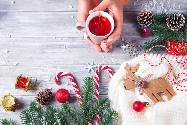 Frau, die in den Händen heißen Weihnachtstee mit Zuckerstange gegen Dekorationen, Geschenkboxen hält