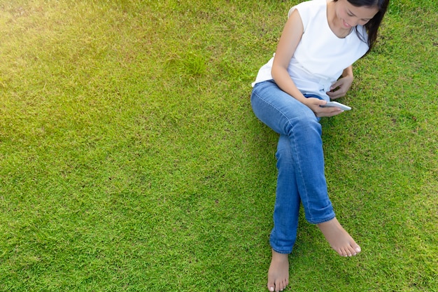 Frau, die intelligentes Mobiltelefon auf dem Gras für die Entspannung mit Social Media verwendet