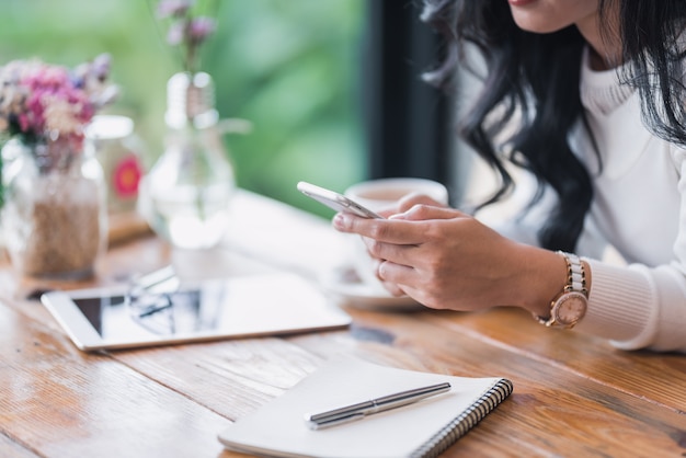 Frau, die intelligentes Telefon mit Kaffeetasse hält und verwendet