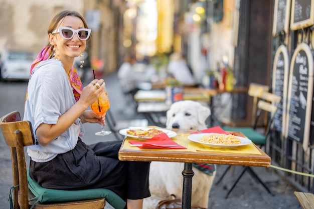 Frau, die italienische Pasta isst, während sie mit einem Hund im Restaurant auf der Straße in Rom sitzt