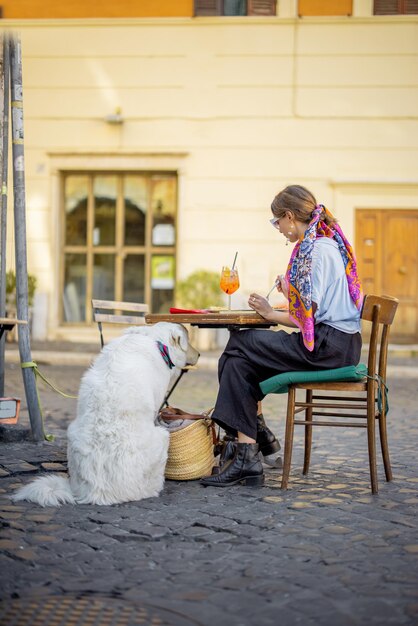 Frau, die italienische Pasta isst, während sie mit einem Hund im Restaurant auf der Straße in Rom sitzt