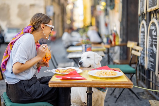 Foto frau, die italienische pasta isst, während sie mit einem hund im restaurant auf der straße in rom sitzt